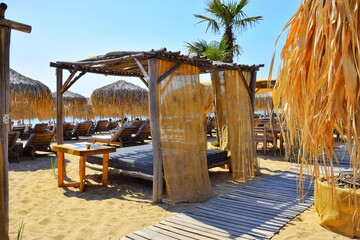 Canopy bed and wooden sun loungers with thatched umbrellas at the beach bar.