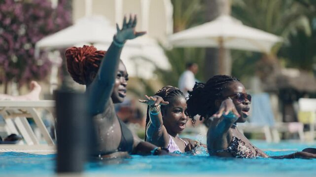Joyful group of black women enjoying a summer vacation at swimming poolside, dancing and sharing good vibes in slow motion