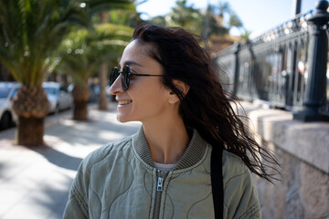 Close-up portrait of a smiling young woman with sunglasses and loose hair, enjoying a sunny day on...