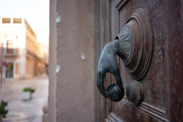 Vintage bronze door knocker in shape of a hand holding a ball on an old wooden door in European...