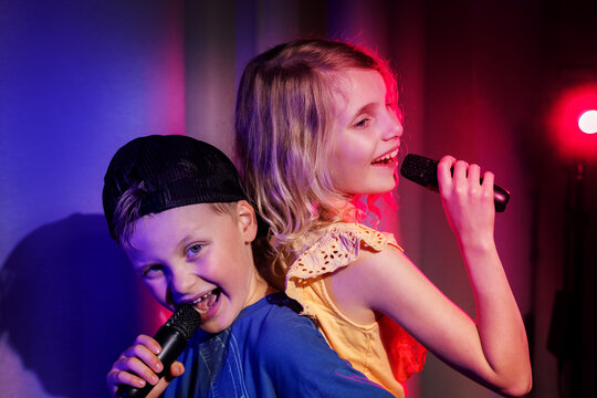 Happy boy and girl duet sing in microphones. karaoke party, children concert performance