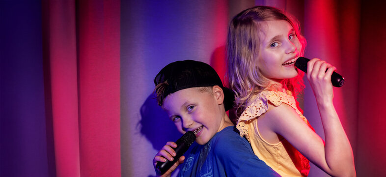 Joyful boy and girl duet sing in microphones. karaoke party, children concert performance. banner with copy space