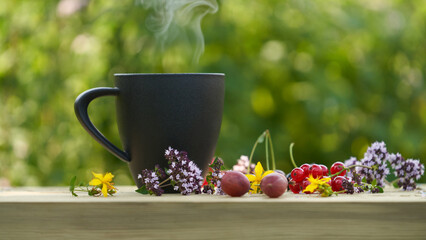 Berry and herbal drink with oregano. Black cup on wooden surface surrounded by oregano...