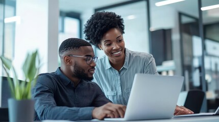 Young male team member learning from black businesswoman in modern office, working on project with laptop, female manager offering help with tech company task