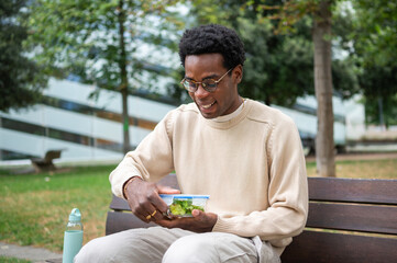 Obraz premium Happy office worker opening lunchbox with healthy salad outdoors during break