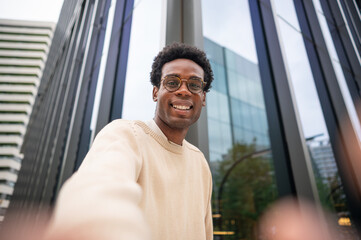 Smiling young man taking selfie in urban setting with modern office buildings