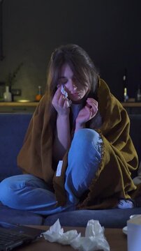Vulnerable and tearful state of woman. Female tearfulness during PMS or pregnancy. Hormonal imbalance. Caucasian woman sits on sofa at home, wrapped in blanket, watches movie, melodrama, cries, sad.