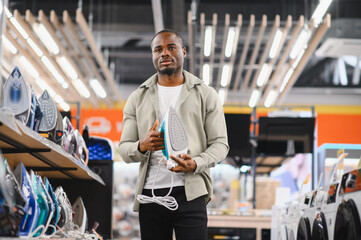 Customer choosing clothes iron in electronics store at mall