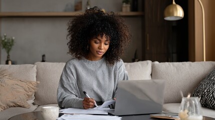 Black woman accountant working from home, focused on bookkeeping spreadsheets and reading detailed financial report on laptop, preparing audit figures and tax return data for efficient asset managemen