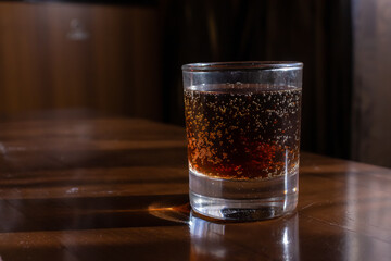 Glass of fizzy drink on wooden table in a dimly lit venue
