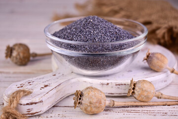 Poppy seeds in a transparent bowl and dried poppy heads, on a white background.
