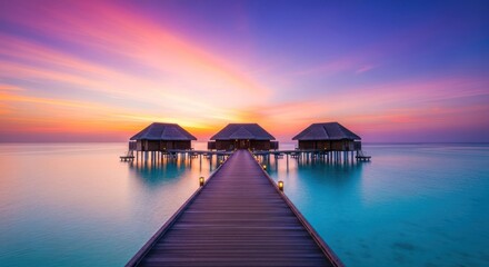 Obraz premium Three huts on stilts connected by a boardwalk over the ocean at a colorful sunset sky horizon