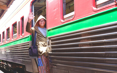 Asian tourist in casual style and camera bag waving hand to friend on train stairs at train station, Perspective side view