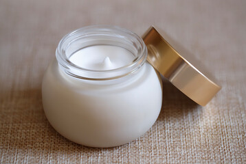 Luxury white cream jar with gold lid in minimalist high-end skincare product display