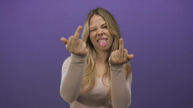 Blonde caucasian woman shows both middle fingers toward camera in purple studio; defiance rebellion anger.