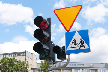 Traffic light with red signal and pedestrian crossing sign. Yield sign above modern street pole....