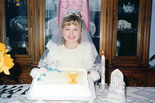 Circa 1995 - Tween girl holds up a cake celebrating her first communion Catholic religion. Vintage scan may have imperfections