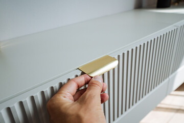 A hand elegantly grasping a modern brass handle, which is attached to stylish and chic grey...