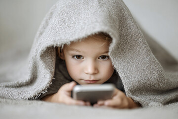 child with digital addiction secretly surfing the internet and playing games hiding under the blanket