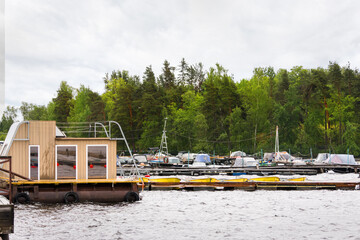 Floating wooden house and pier with boats lined up in order on lakeside shore waiting near green...