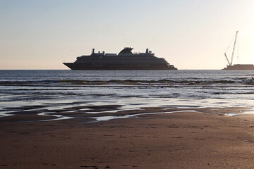 Cruise ship near the shore at low tide with wide sand and shallow water in foreground. Calm coastal...