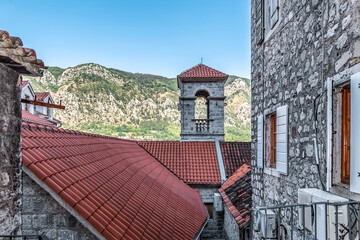 Picturesque view of red-tiled rooftops in Kotor, Montenegro, with a bell tower framed by stunning...