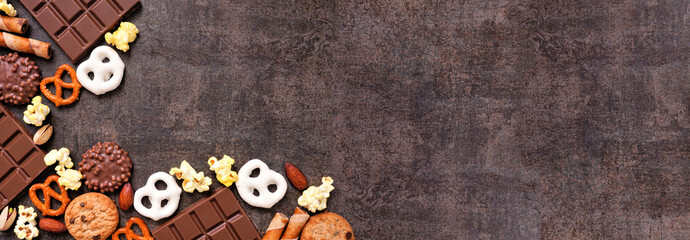 Sweet and salty snacks corner border over a dark banner background. Chocolate, popcorn, pretzels, nuts and cookies. Overhead view.