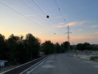 High voltage power line pylon with large balls hanging on power line to warn pilots, low flying planes and helicopters against sunset sky
