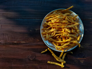 A bowl of crispy yellow snack sticks placed on a wooden table.