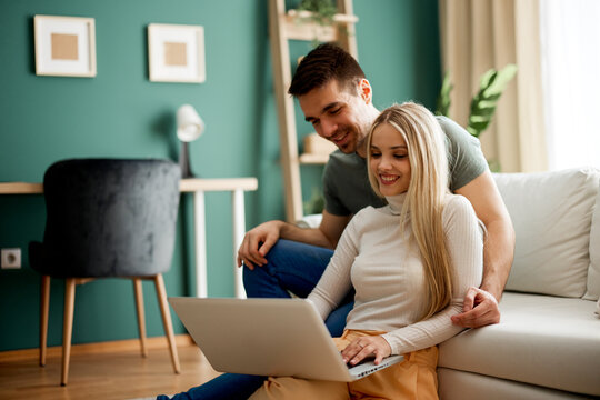 Happy couple using laptop, browsing internet at home