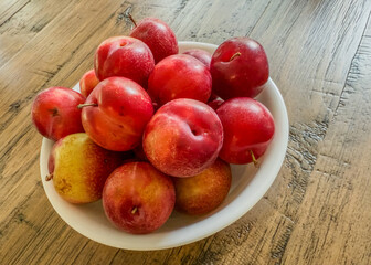 Small, juicy cherry plums in a white bowl on a wooden table top