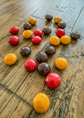 Candy shell coated chocolates in red, yellow, and brown on a wooden table