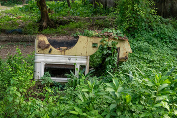 Overgrown abandoned vehicle wreck amidst lush green foliage in an outdoor environment shows nature...