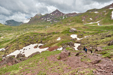 Fototapeta premium Family walking in the mountains with cloudy skies and snowdrifts. Pyrenees
