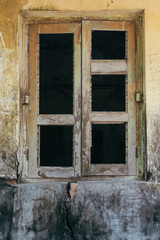 Old wooden window with broken glass and weathered wall shows decay and disrepair from a bygone era...