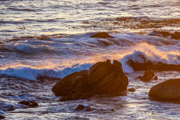 Golden sunset light washes over crashing waves and sea-swept rocks