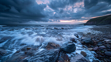 A rocky beach with crashing waves under a dramatic cloudy sky at dusk with land in the background