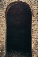 An arched doorway crafted from weathered stone stands open, revealing a shadowy interior and an...