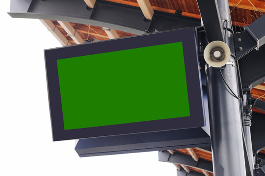 Blank digital screen on train station. Green chroma key background for message or timetable. Display under roof with speaker. Public transport infrastructure. Mockup for travel information display.