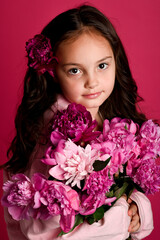 A young girl of Caucasian descent holds a bouquet of vibrant pink flowers against a pink backdrop,...