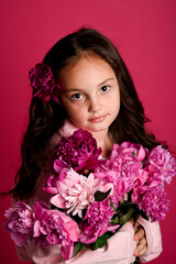 A young girl of Caucasian descent holds a vibrant bouquet of pink flowers against a pink background.