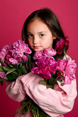 A young girl of Hispanic descent holds a bouquet of pink flowers, exuding a sense of innocence and...