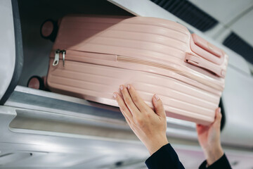 hands placing pink carry on luggage bag securely in overhead storage compartment airplane cabin preparing travel journey flight departure © Freedomz