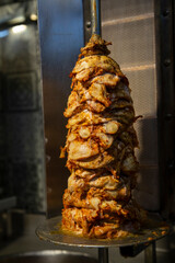 Succulent chicken shawarma rotating on a vertical spit, sizzling in a stainless steel kitchen,...