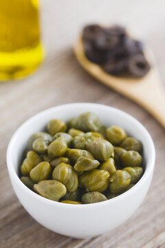 Pickled capers in small bowl with black olive slices and olive oil in the back, the ingredients for the French tapenade spread (Selective Focus, Focus one third into the capers) 