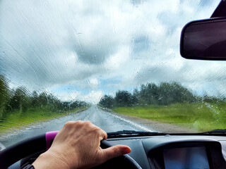 Car salon, windshield, hand of woman on steering wheel and landscape. View from seat of driver on...