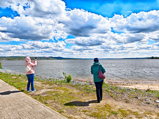 Visitors enjoy a sunny day by the waterfront gazing at the scenic river and dynamic clouds in the...
