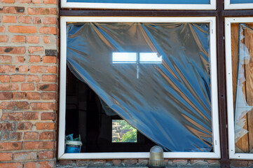 A weathered window with a plastic cover flaps slightly in the breeze, revealing a hint of greenery...