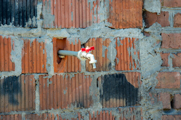 A water faucet is protruding from a brick wall at a construction site, illuminated by natural...