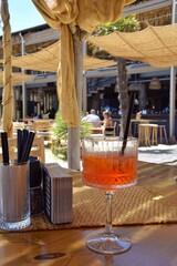 A glass of Aperol Spritz on a table at a beach bar.